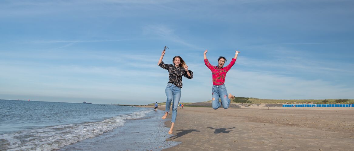 Twee studenten springen in de lucht op het strand