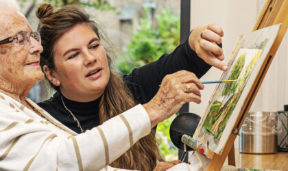 Social Work student werkt samen met oude vrouw in rolstoel aan een schilderij
