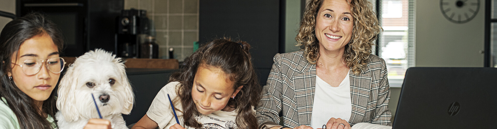 Deeltijd student is aan het studeren aan de eettafel met haar knutselende kinderen en hond