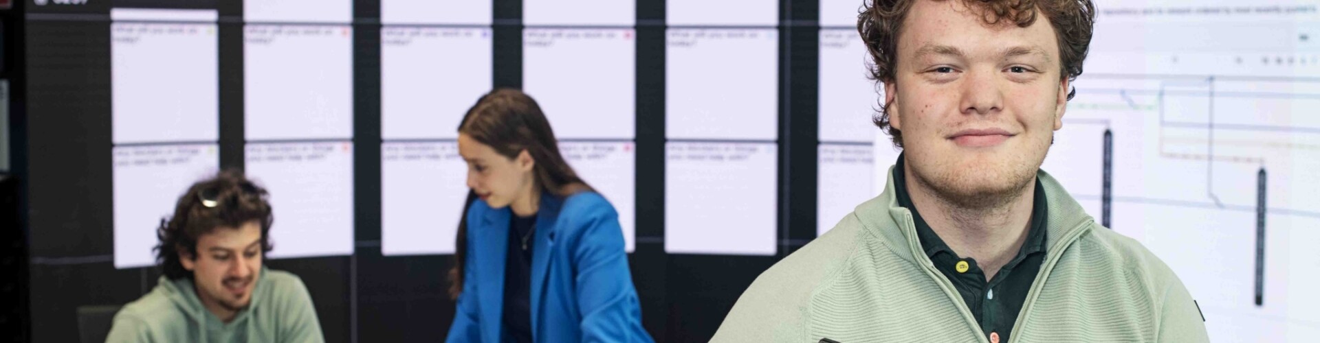 ICT student met een laptop in zijn handen en andere studenten op de achtergrond