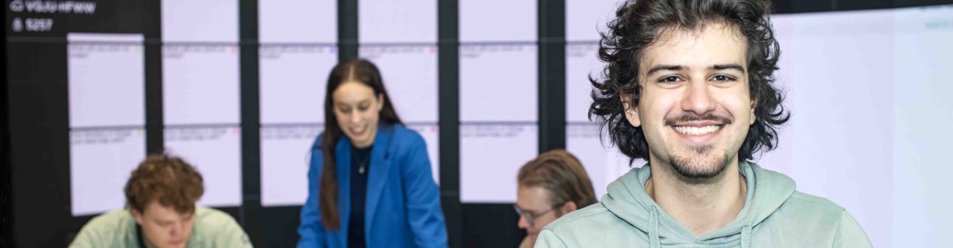 ICT student met op de achtergrond andere studenten die samen aan het werk zijn