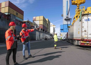 Two Logistics Engineering students with a large container ship behind them