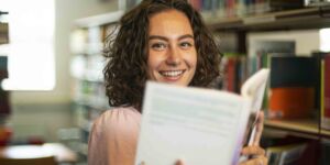 Portret van Pedagogiek student in de mediatheek met een boek in haar handen