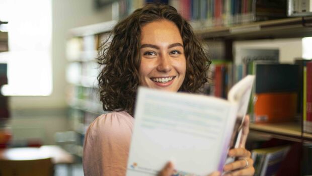 Portret van Pedagogiek student in de mediatheek met een boek in haar handen