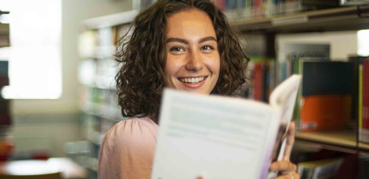 Portret van Pedagogiek student in de mediatheek met een boek in haar handen
