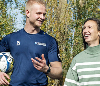 Sportkunde student met een bal onder zijn arm praat met een vrouw in een groene omgeving