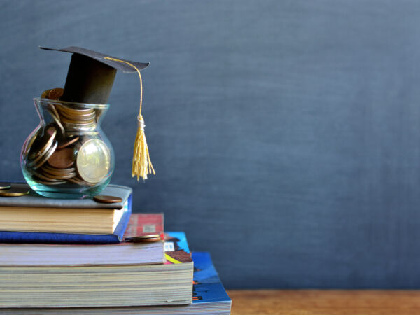 Stapel boeken met een potje geld en een afstudeercap