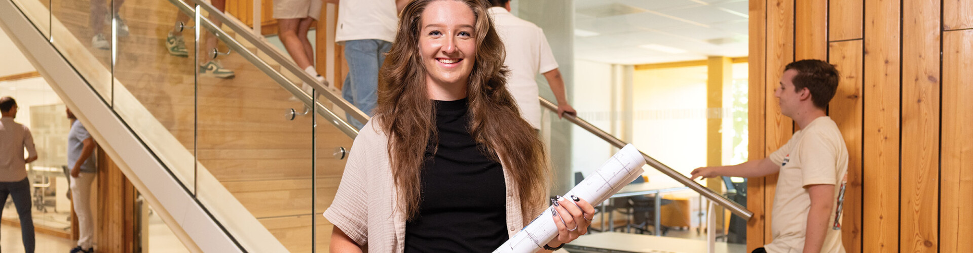 Desirée staat bij een houten trap in het HZ-gebouw met een bouwtekening in haar handen.