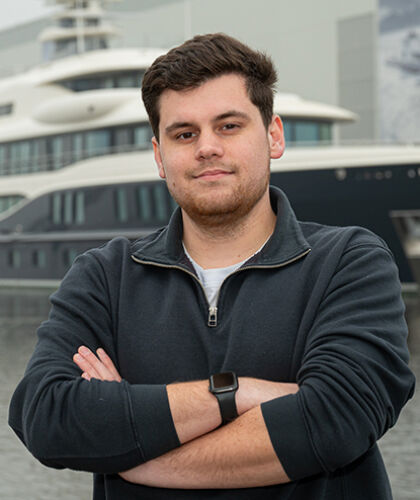 HZ-student Rens poseert op de kade van zijn maritieme werkplek, met op de achtergrond een schip.