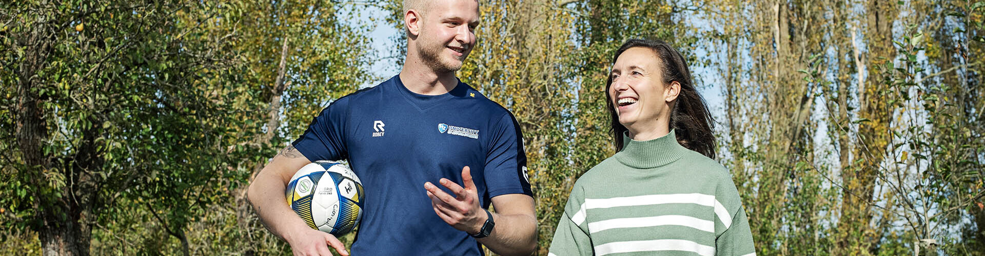 Sportkunde student met een bal onder zijn arm praat met een vrouw in een groene omgeving