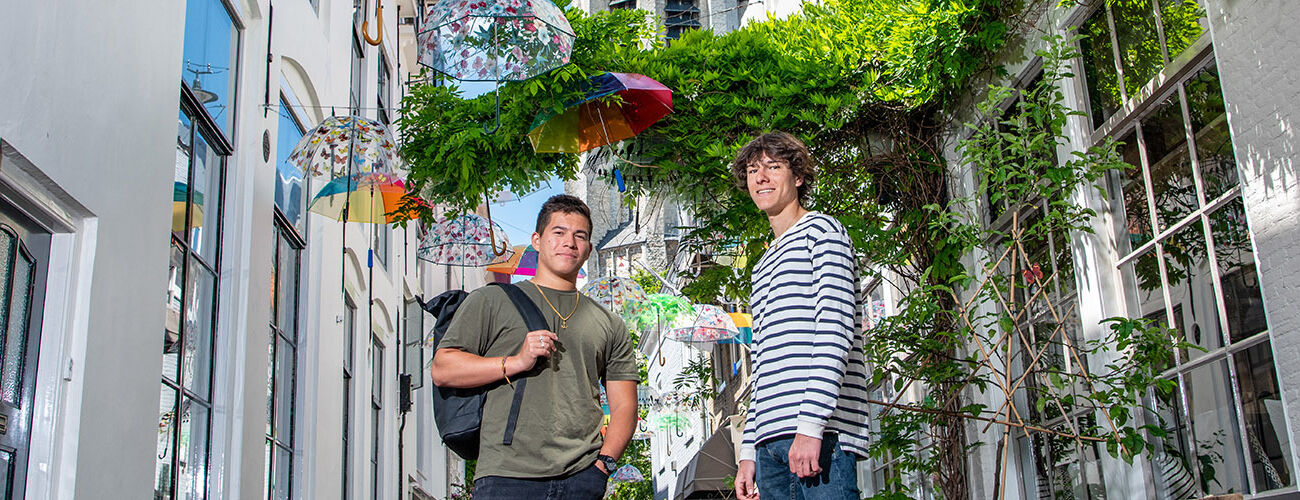 Two male international students standing in the middle of the photogenic street in Middelburg with colourful umbrella's