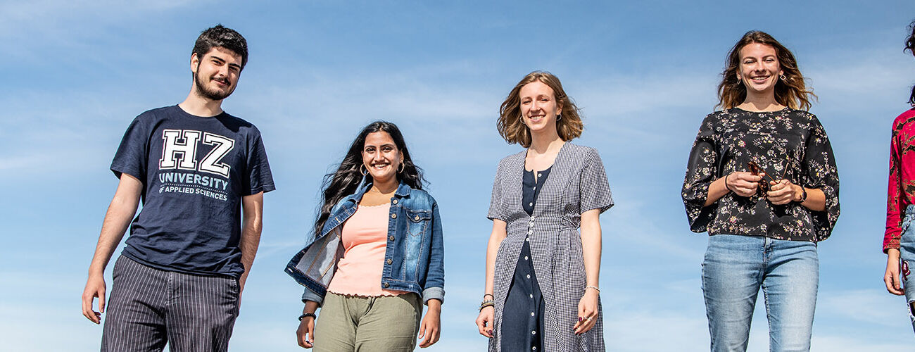 A group of five international students of HZ University of Applied Sciences standing and smiling in front of a blue sky.