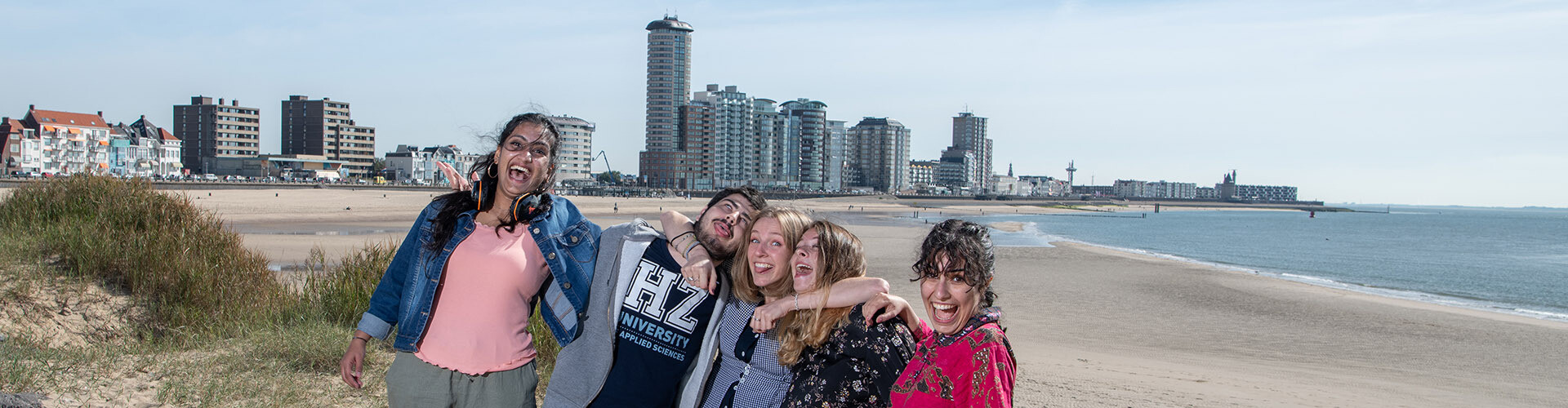 Five international students making friends and having fun together at the beach with the city of Vlissingen, Zeeland, The Netherlands in the background.