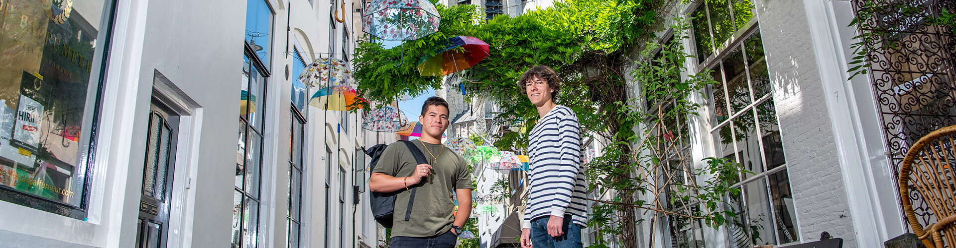 Two male international students standing in the middle of the photogenic street in Middelburg with colourful umbrella's