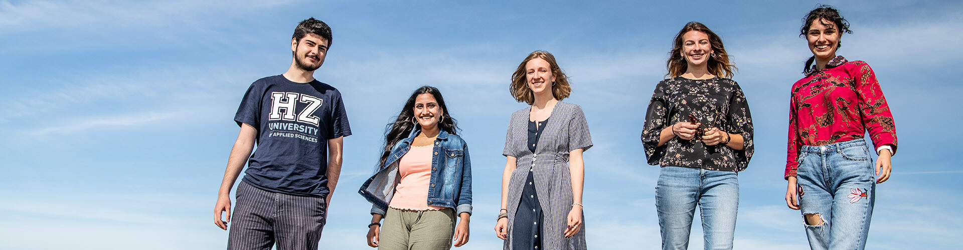 A group of five international students of HZ University of Applied Sciences standing and smiling in front of a blue sky.