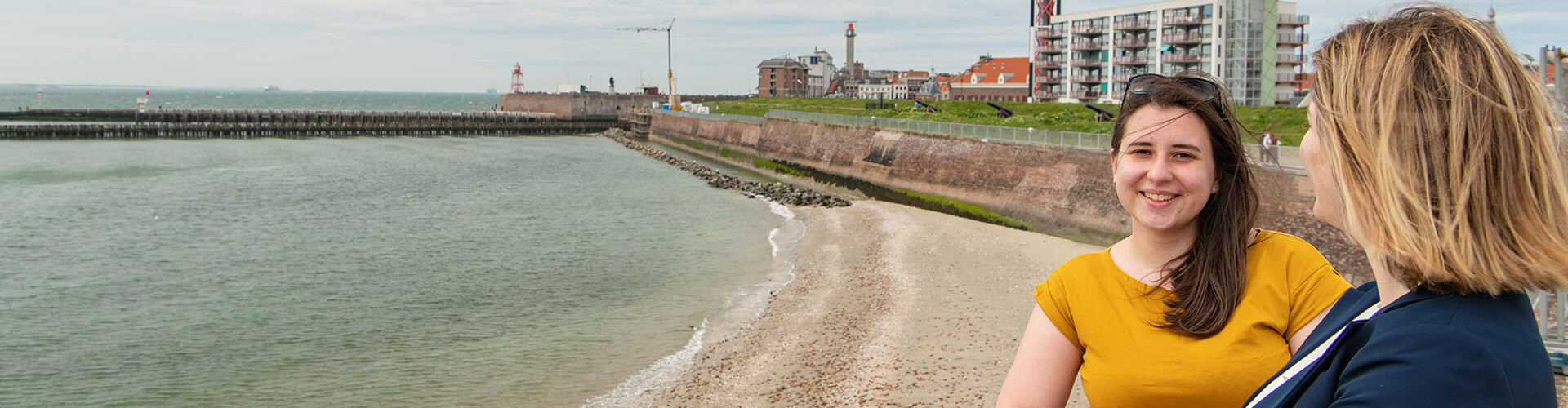 Two female international students are looking over the sea with the skyline of Vlissingen, Zeeland, The Netherlands, in the background/