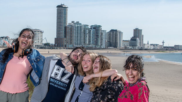 Five international students making friends and having fun together at the beach with the city of Vlissingen, Zeeland, The Netherlands in the background.