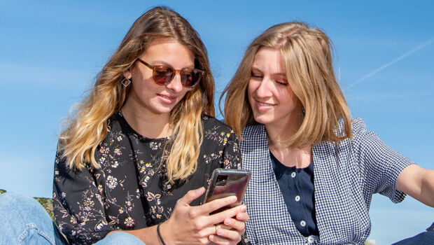 Two female international students sitting on the beach in Zeeland, the Netherlands, looking at student jobs on their phone.