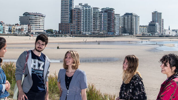 A group of international students, who study at HZ University of Applied Sciences, laughing an talking in the dunes of the beach at Vlissingen, Zeeland, The Netherlands, with the sky line of sea and the City of Vlissingen in the background.