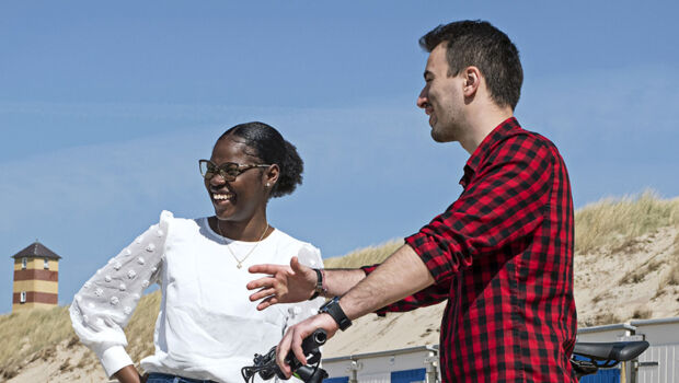 Three international students (one girl and two boys) are talking and enjoying themselves at the beach in Vlissingen, Zeeland, the Netherlands with the dunes and lighthouse in the background.