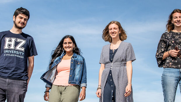 A group of five international students of HZ University of Applied Sciences standing and smiling in front of a blue sky.